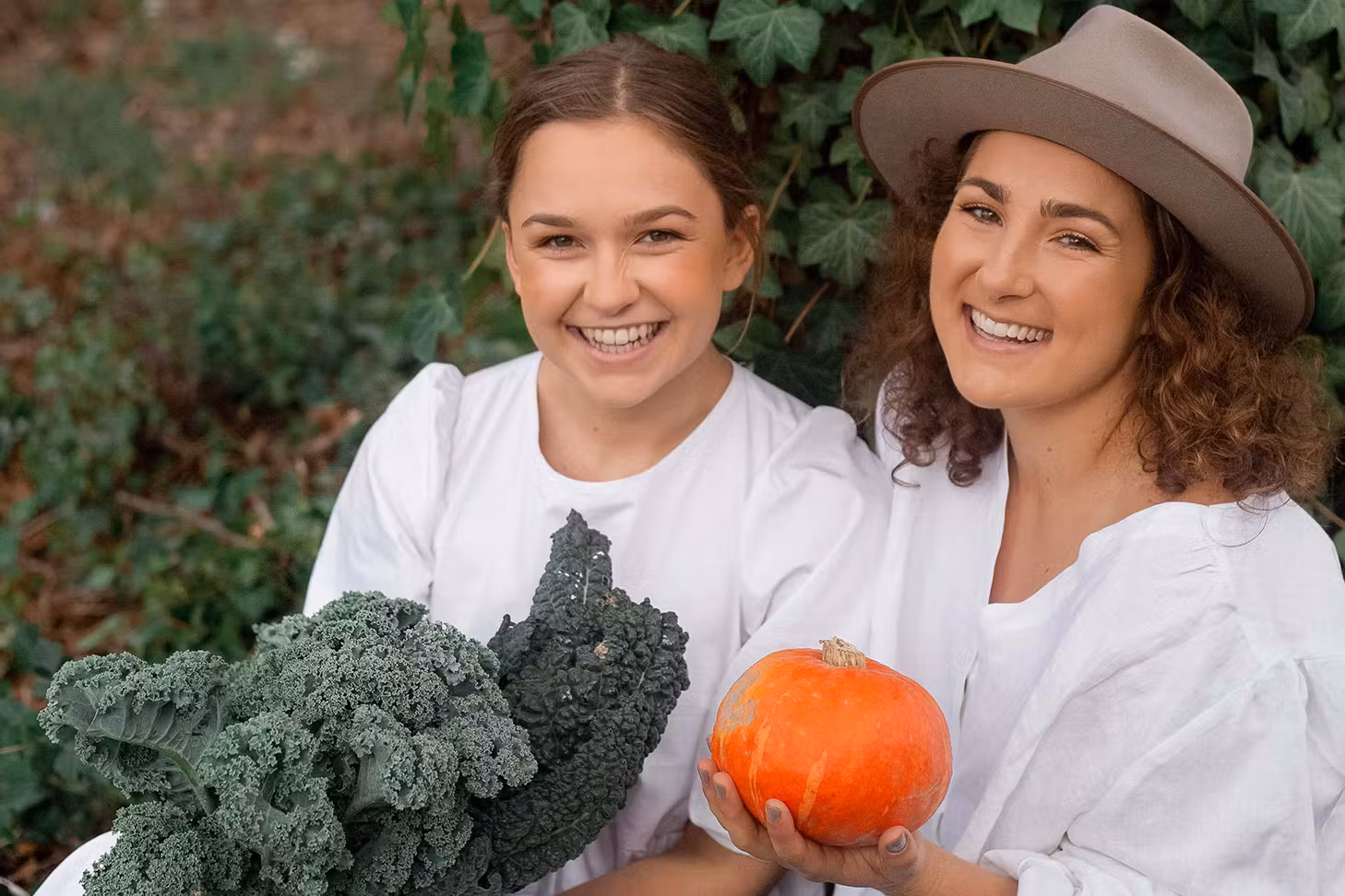 Rosa and Margo from Two Raw Sisters smile at the camera while holding fresh produce.